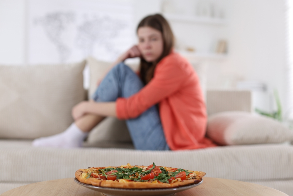 Eine Frau sitzt auf dem Sofa und schaut auf eine Pizza vor ihr.