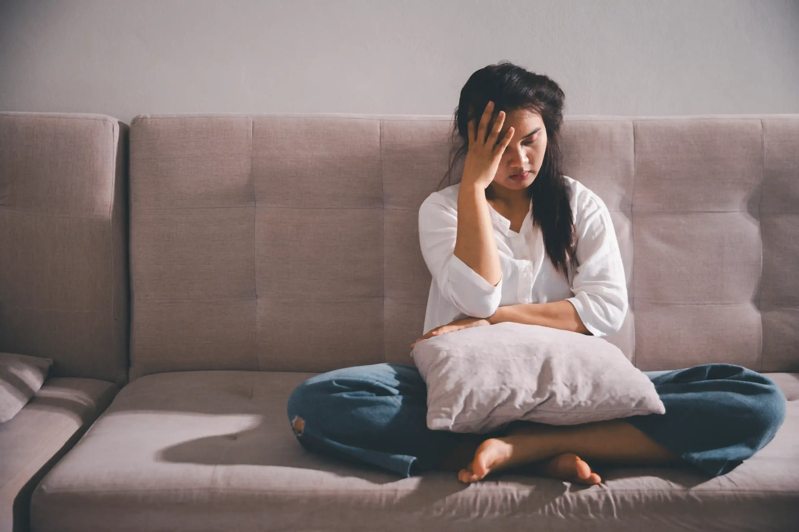 Frau sitzt nachdenklich auf dem Sofa und hält sich den Kopf – Symbolbild für Stress, Überforderung oder depressive Verstimmung.